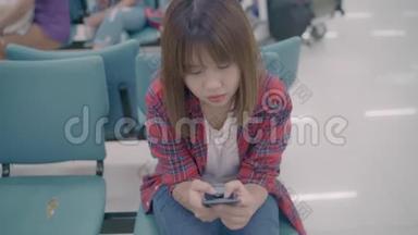 快乐的亚洲女人在机场登机口等待航班时，在<strong>候机大厅</strong>使用和检查她的智能手机。